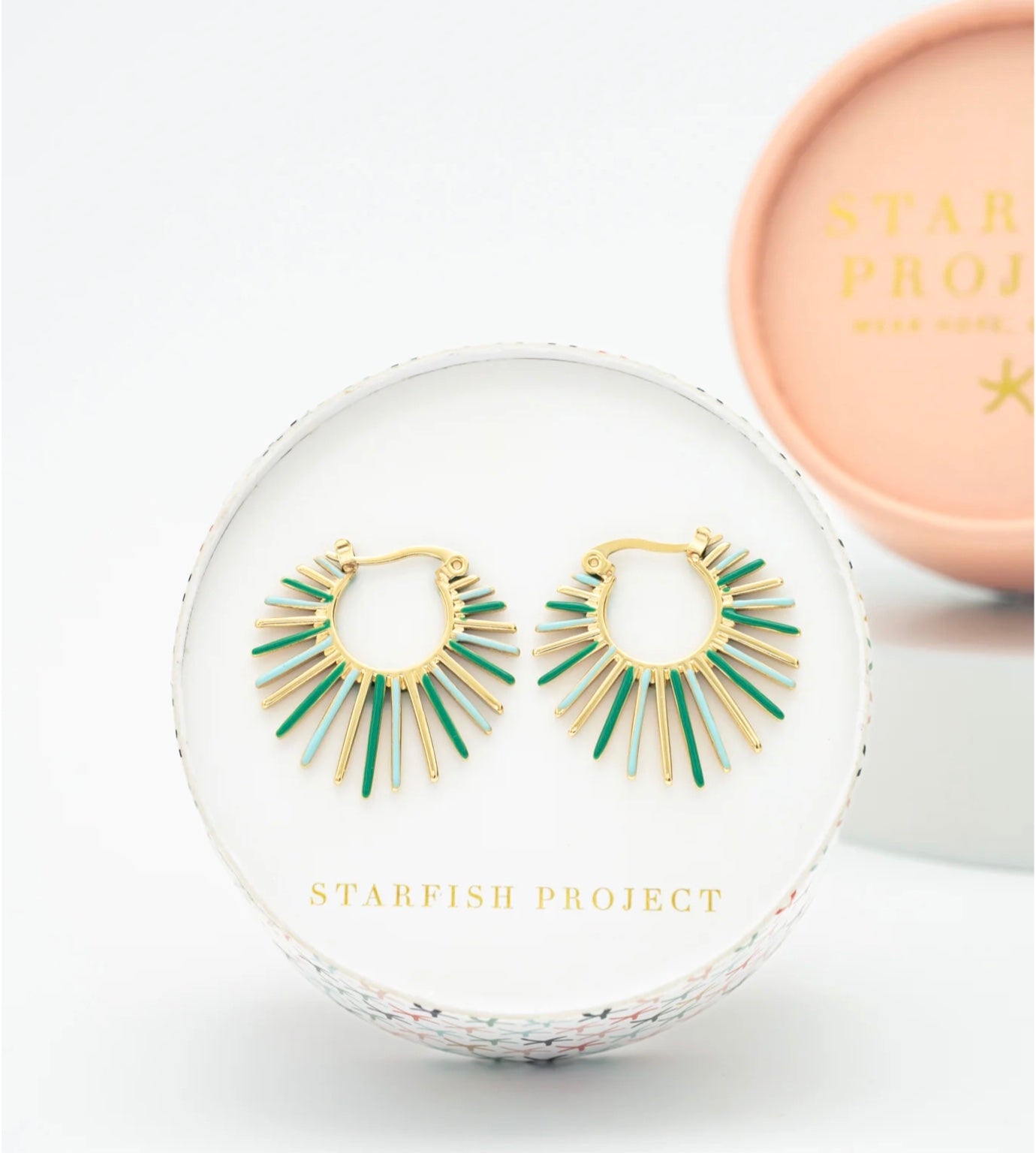 Gold and green earrings in a clear display case with 'Starfish Project' branding.