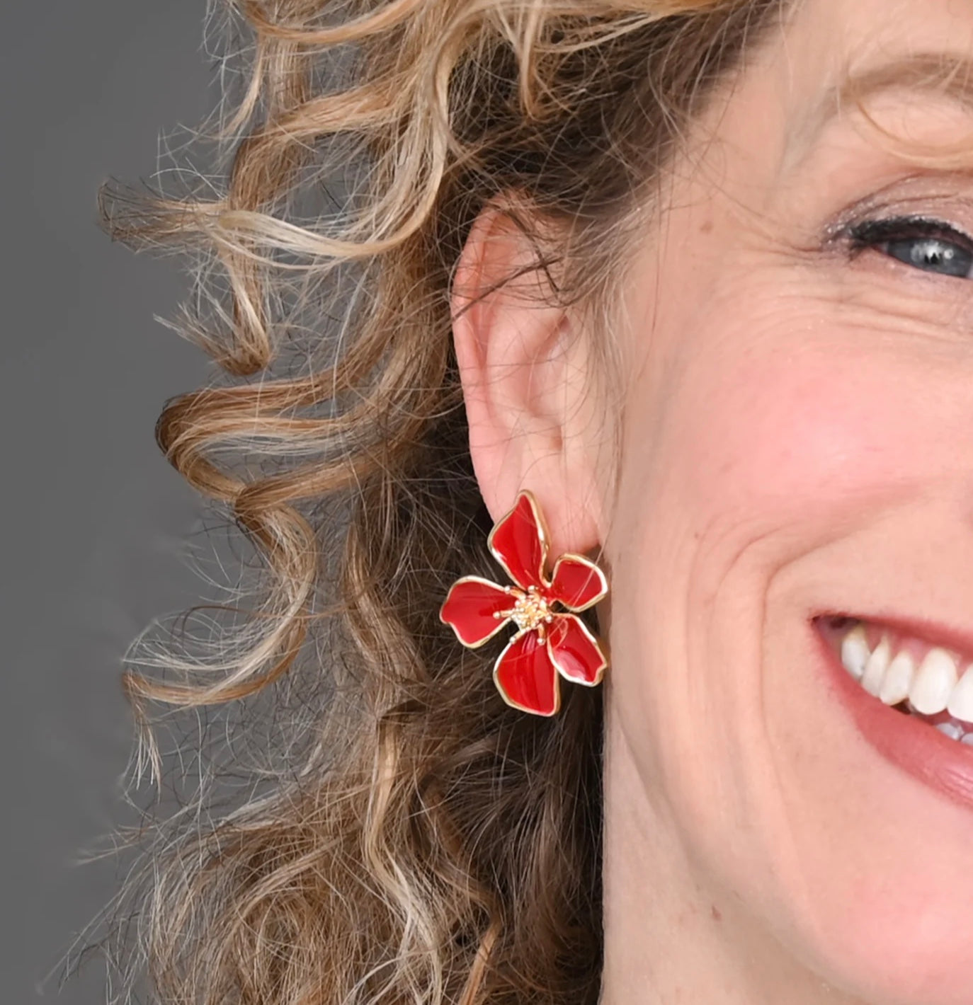 Close-up of a woman wearing a red flower-shaped earring with a gray background