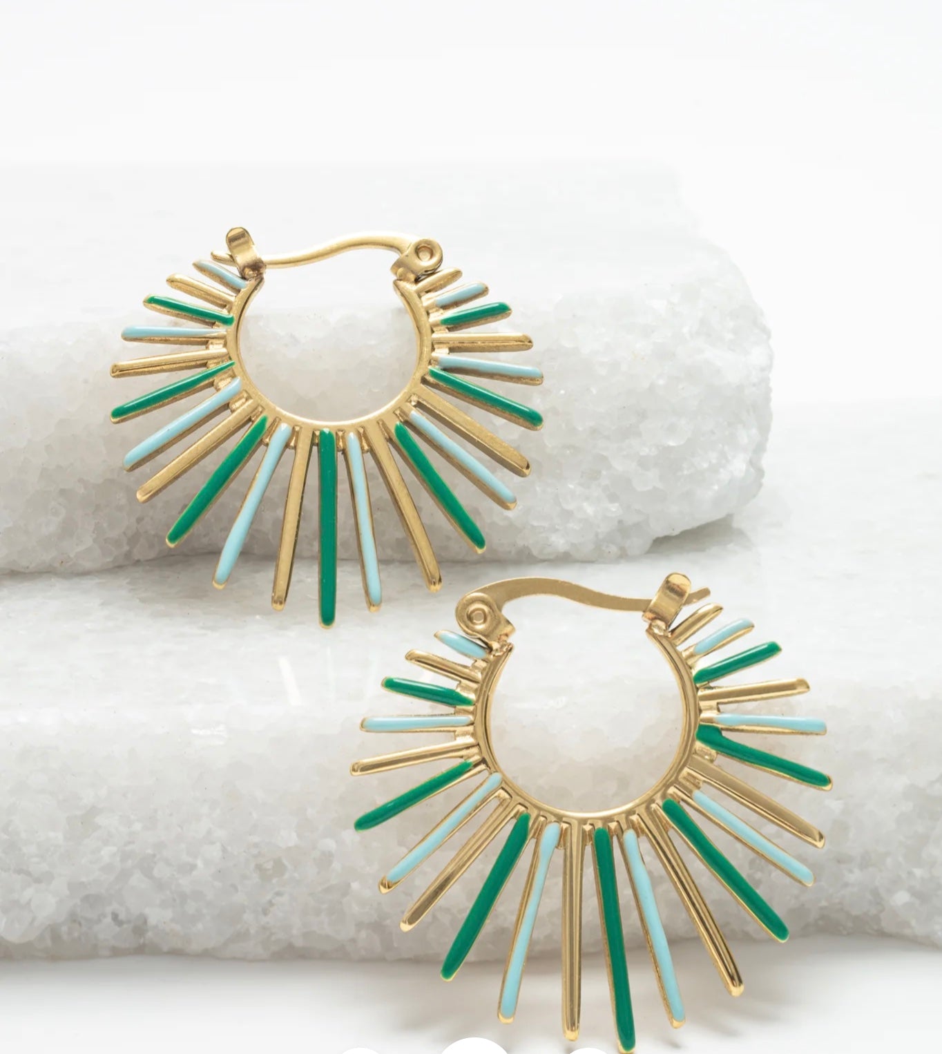 Gold and green sunburst earrings on a white stone background