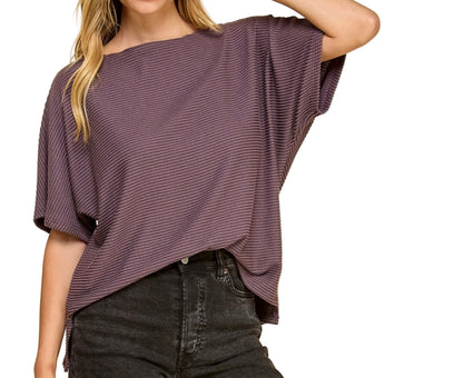 Woman wearing a loose-fitting purple top and black pants on a white background