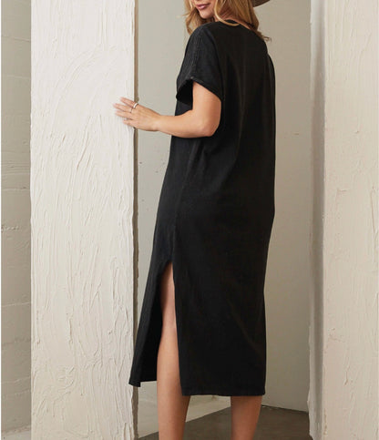 Person wearing a black dress with a slit, standing against a neutral wall.