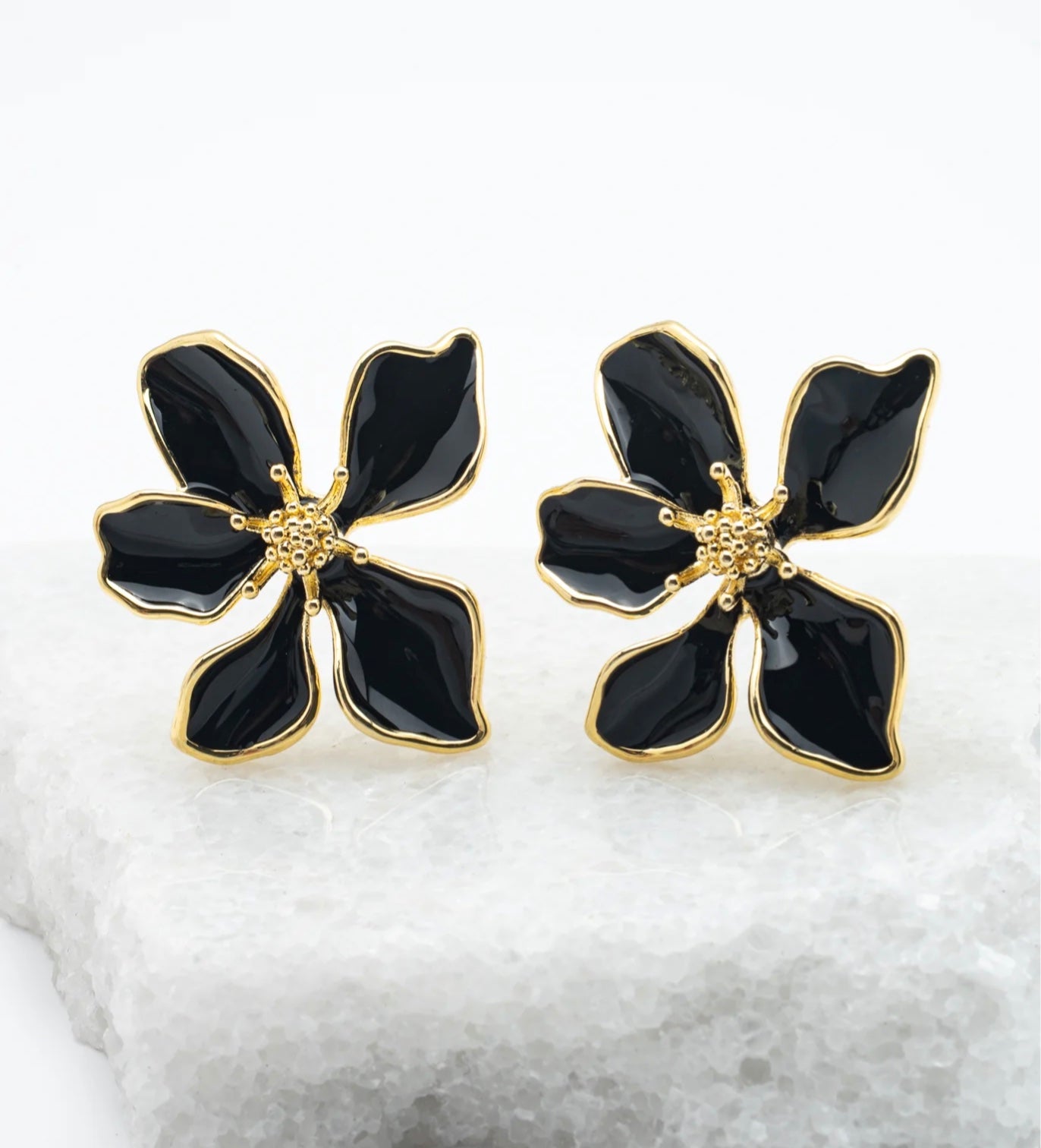 Black flower-shaped earrings with gold accents on a white background