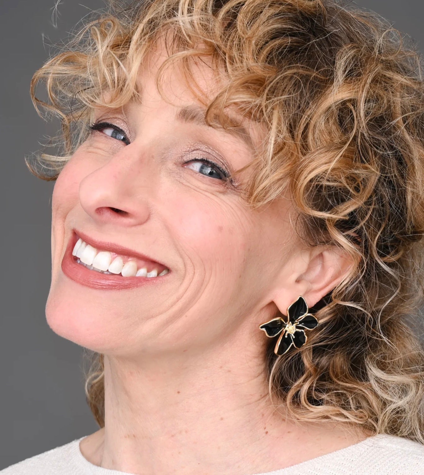 Woman with curly hair wearing a black flower earring against a gray background
