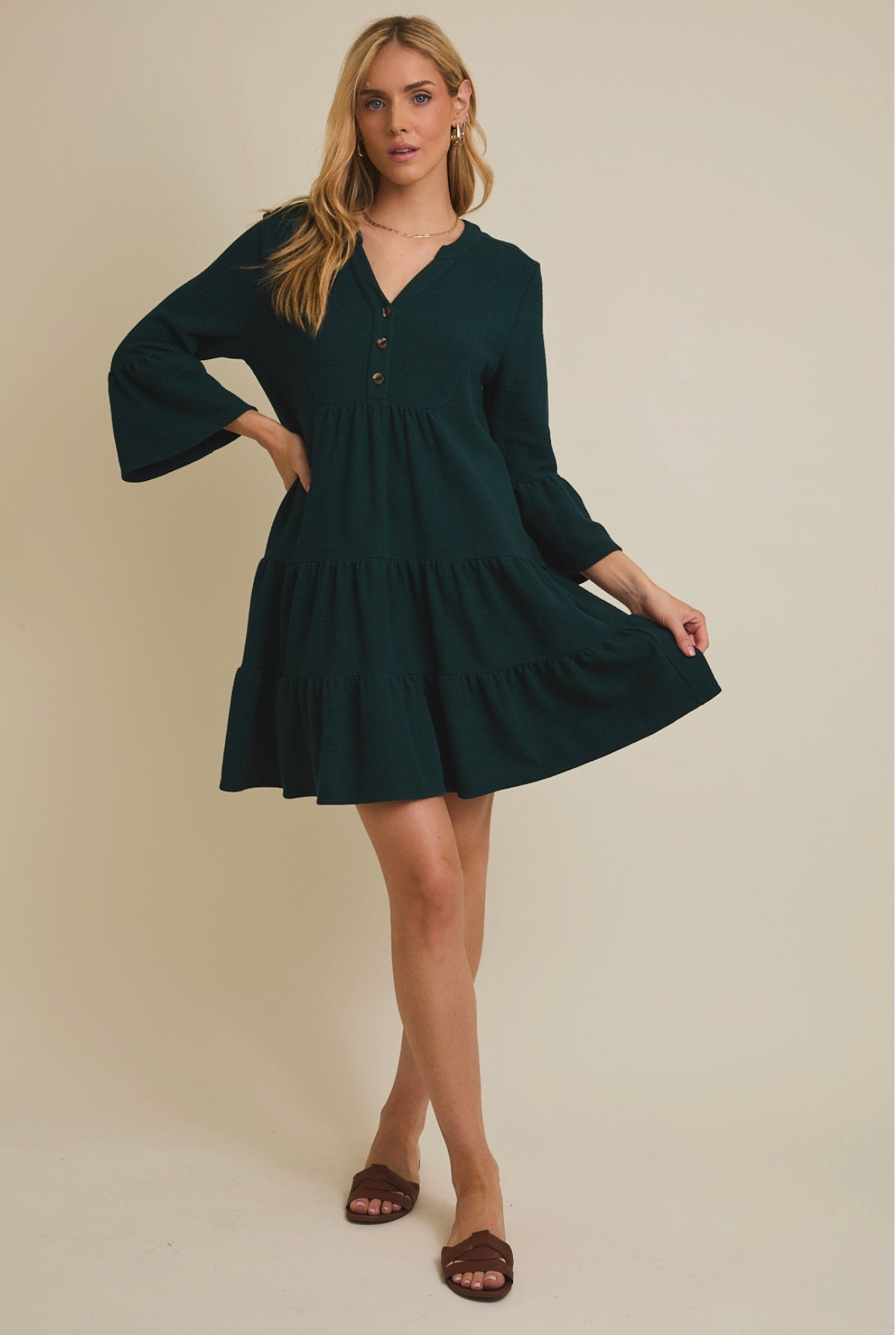 Woman wearing a dark green dress with bell sleeves against a beige background