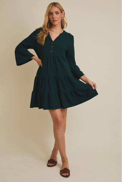 Woman wearing a dark green dress with bell sleeves against a beige background