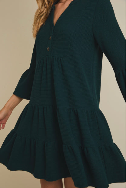 Dark green dress with tiered skirt and long sleeves on a neutral background