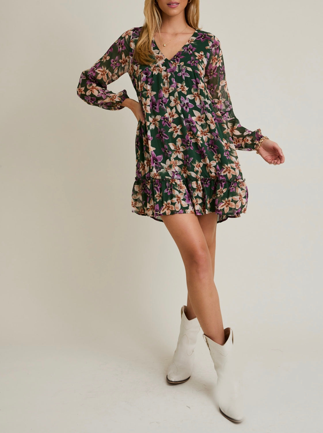 Woman wearing a floral dress with long sleeves and white boots on a plain background