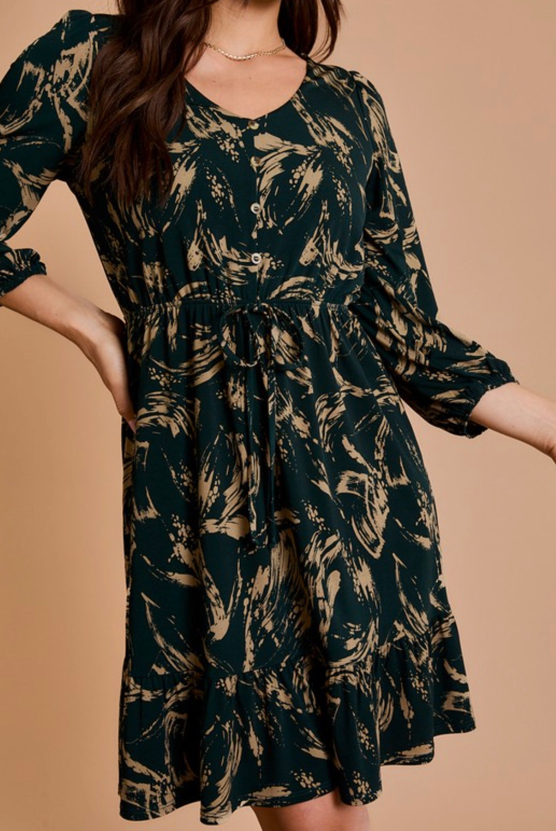 Woman wearing a dark green dress with a leaf pattern on a beige background