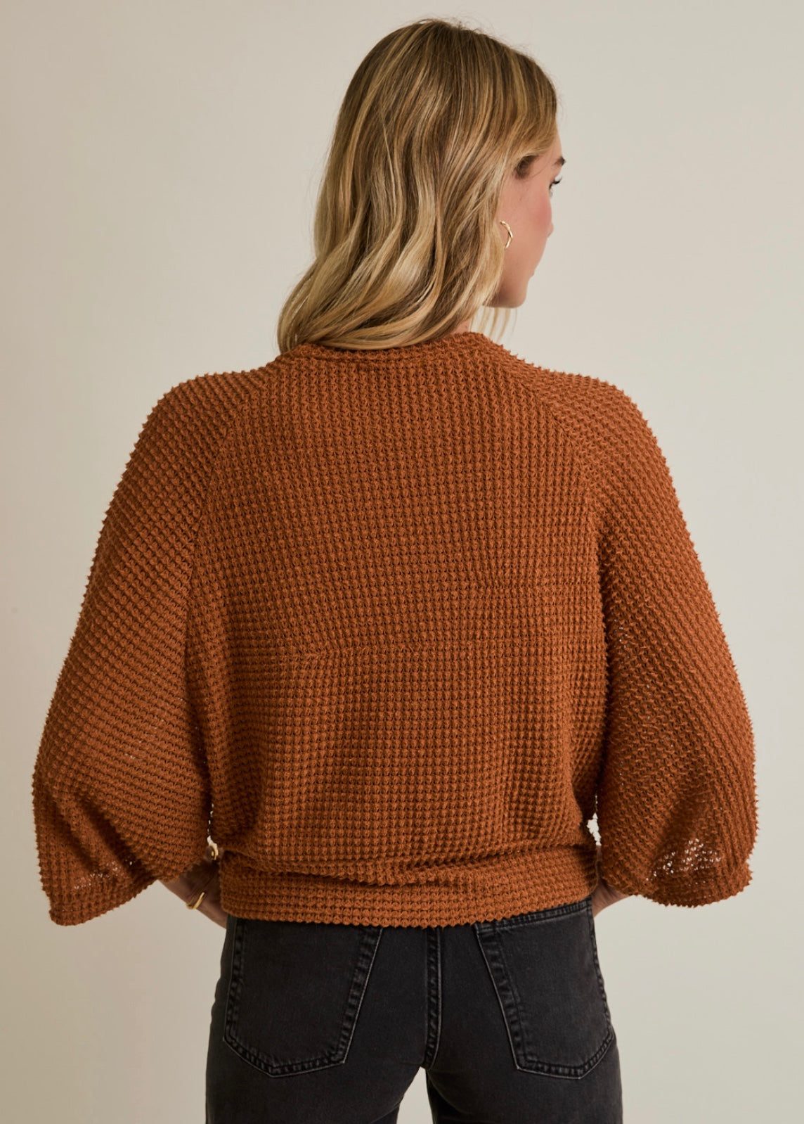 Woman wearing a brown textured sweater against a neutral background