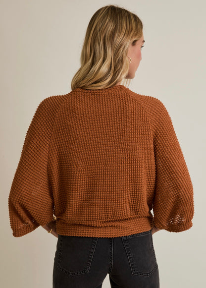 Woman wearing a brown textured sweater against a neutral background