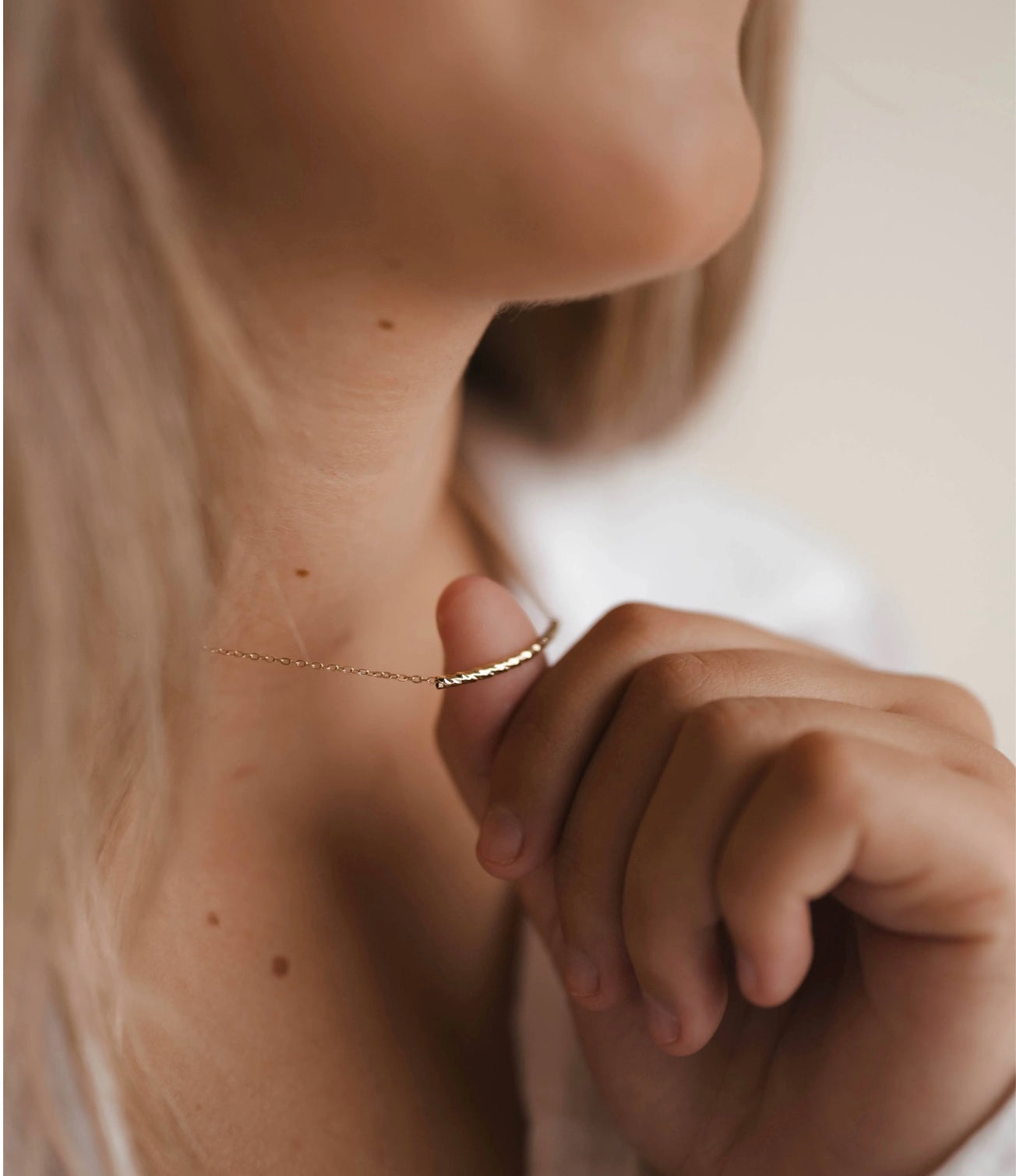 Close-up of a person wearing a delicate gold necklace with a blurred background
